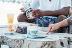 Image displays two friends hands playing Uno by the pool on a wooden coffee table while drinking relaxedfx chill Elixr in a glass. They also have grapes on the table for enjoyment 